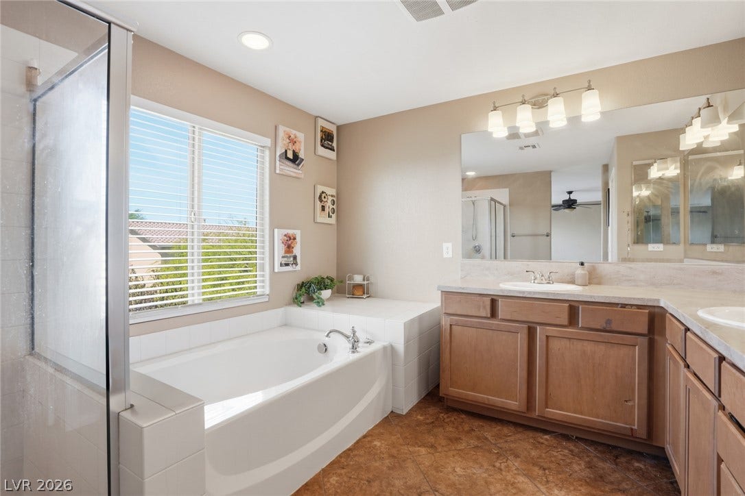 2607 Fading Night Court, Las Vegas, NV 89142 Earth-toned flooring and classic wood cabinetry surround a built-in soaking tub beneath natural window light.