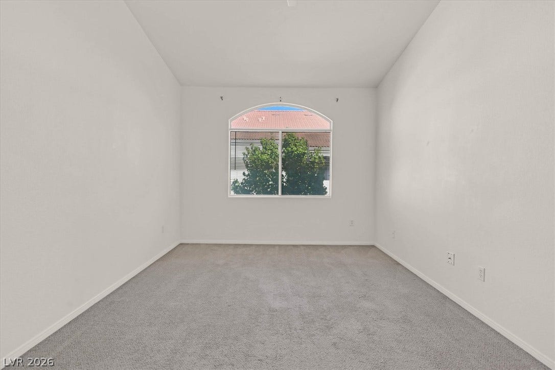 700 Carnegie Street, #2924, Henderson, NV 89052 An arched window frames serene leafy views across this carpeted bedroom.