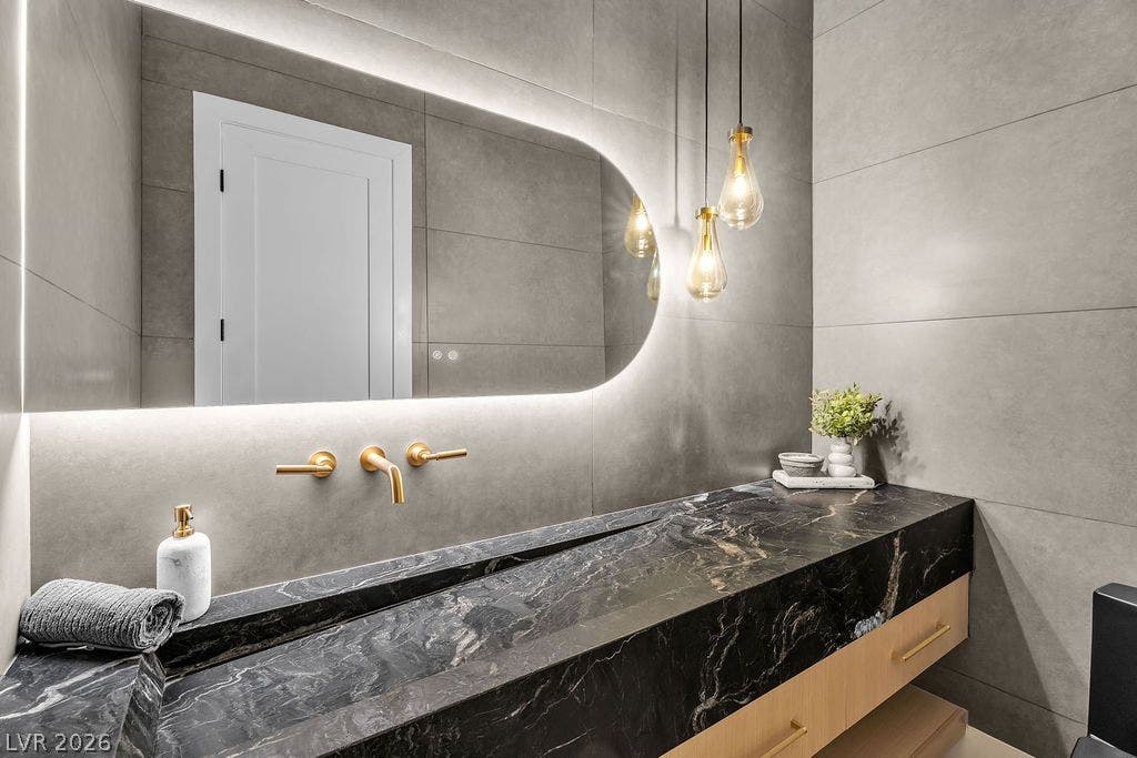 2690 Grassy Spring Place, Las Vegas, NV 89135 Textured gray wall tiles surround a dramatic dark marble vanity with integrated sink and brass fixtures.