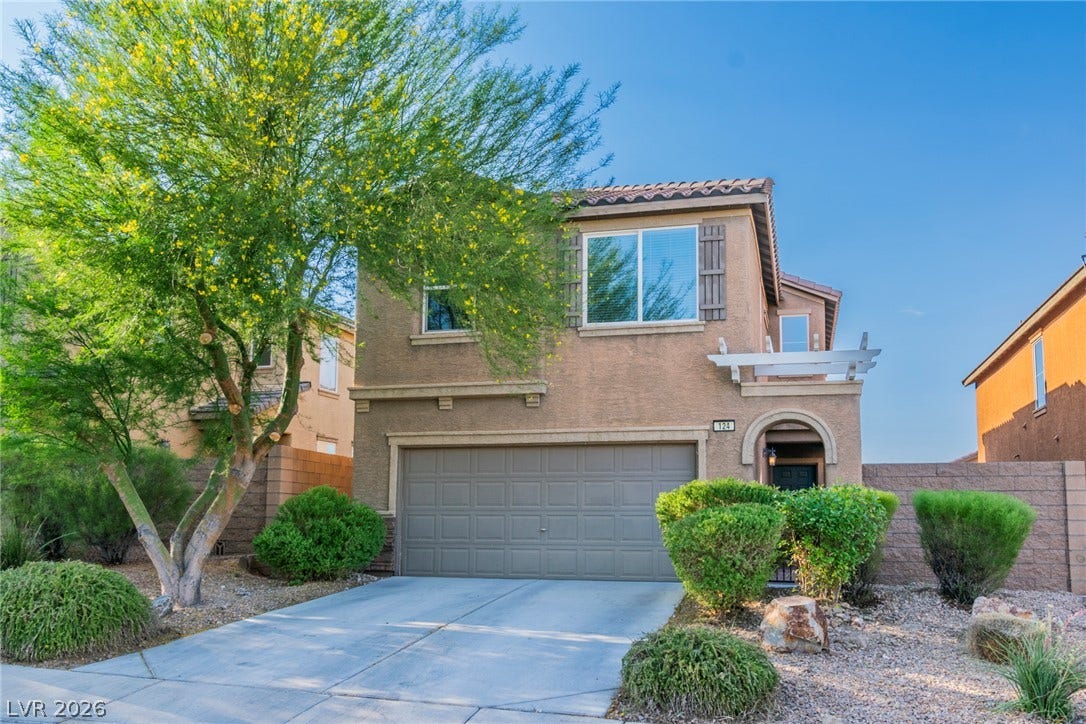 Desert landscaping and a paved driveway frame this stucco home with an attached garage.