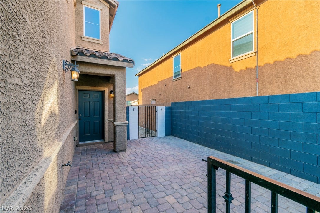 Brick pavers line the private entryway nestled between stucco exterior walls and a fenced courtyard.