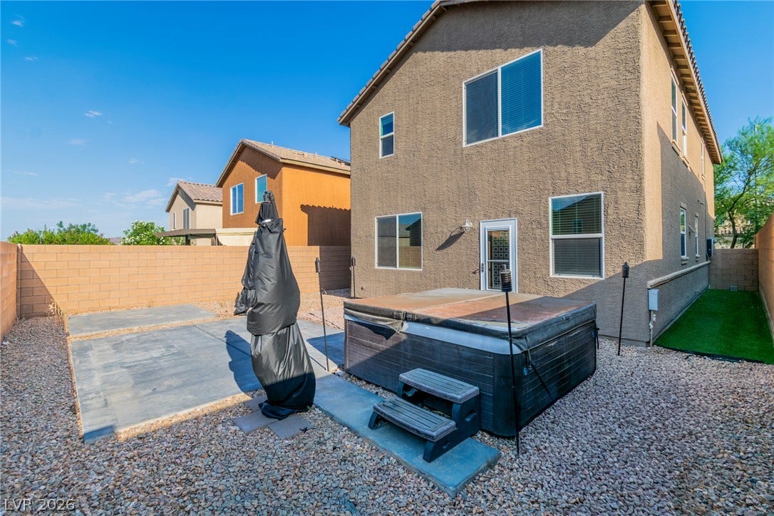 Concrete patios and gravel landscaping surround a two-story home featuring a backyard spa installation.