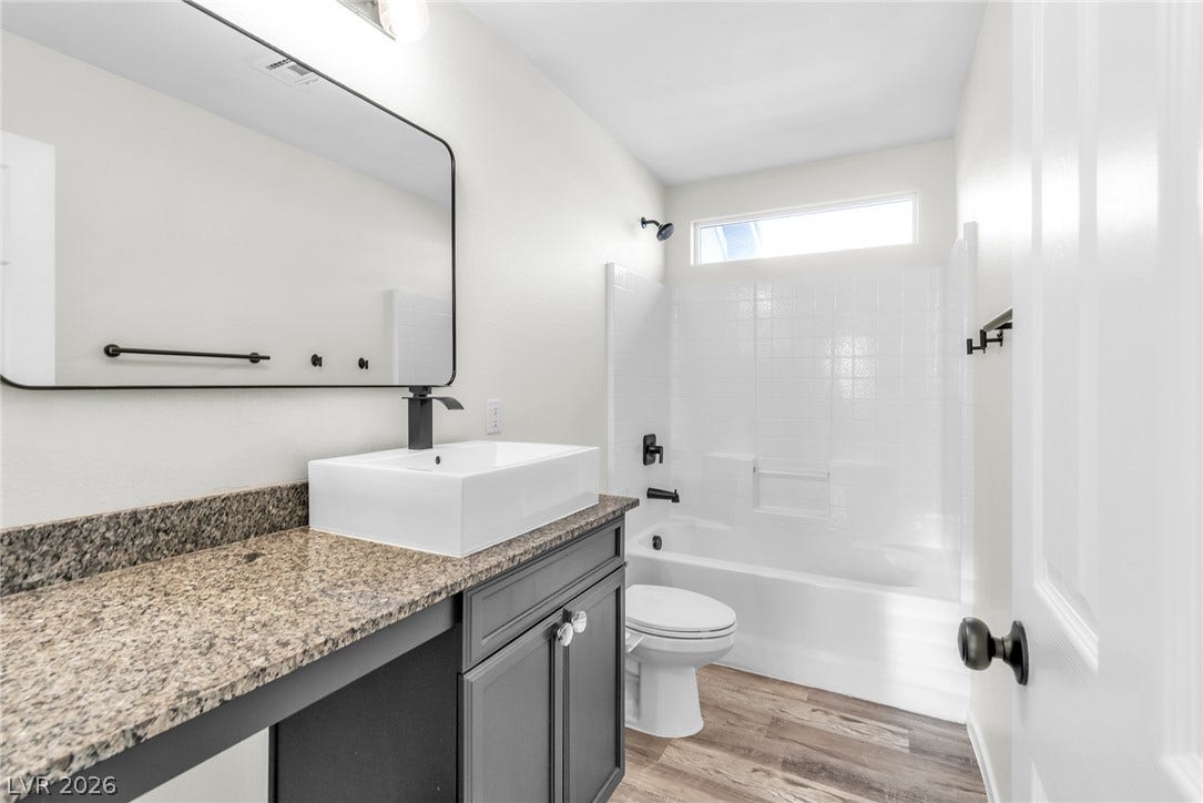Polished granite counters and wood-look flooring elevate this modern full bathroom.