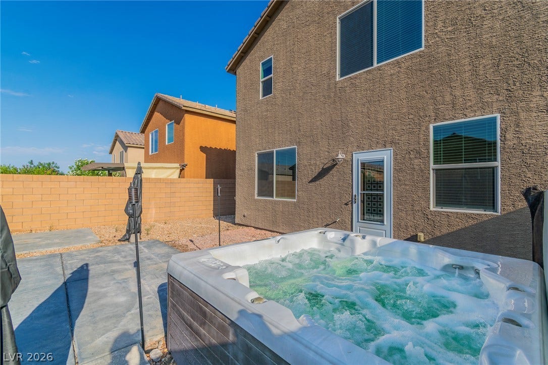 An inviting hot tub centers the paved patio alongside the stucco exterior wall.
