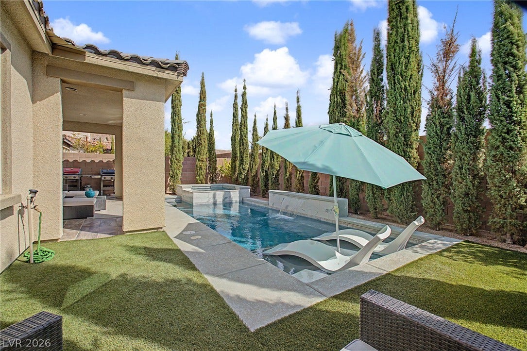Manicured turf borders a shimmering swimming pool with built-in lounge seating and water features.