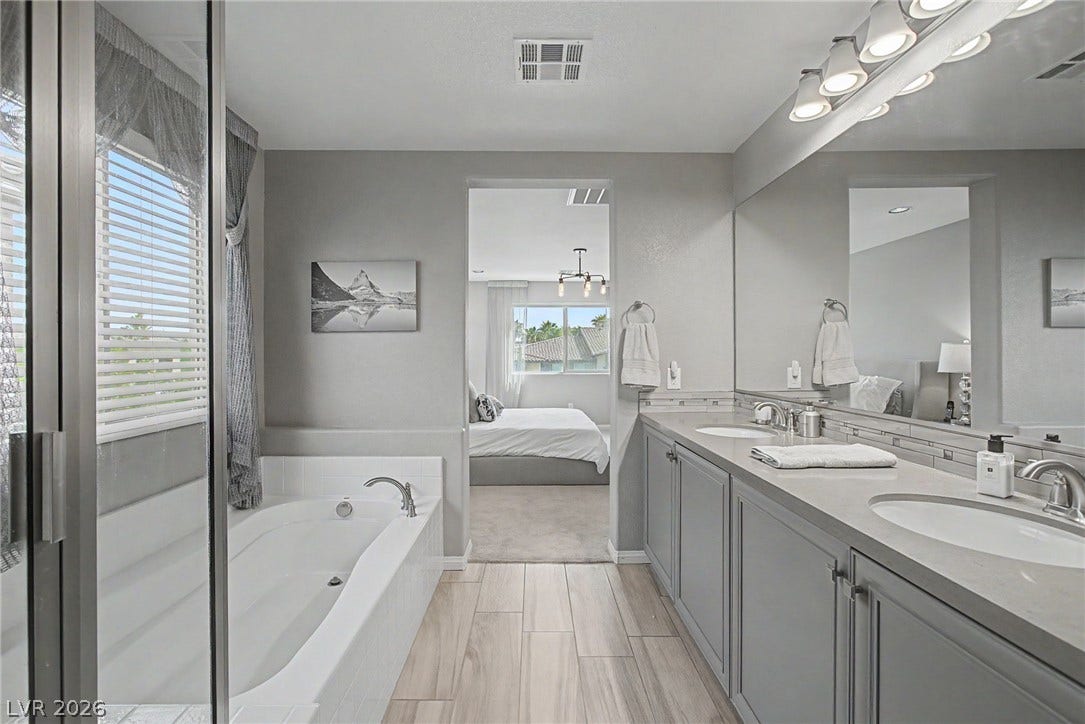 Wood-look tile flooring and a double vanity define this bathroom leading to the bedroom.