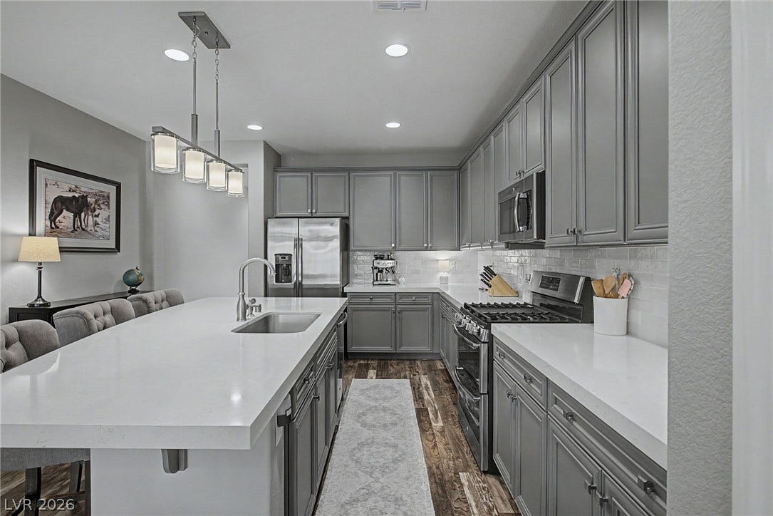 Polished stone countertops complement gray shaker cabinetry and hardwood flooring in this gourmet kitchen.