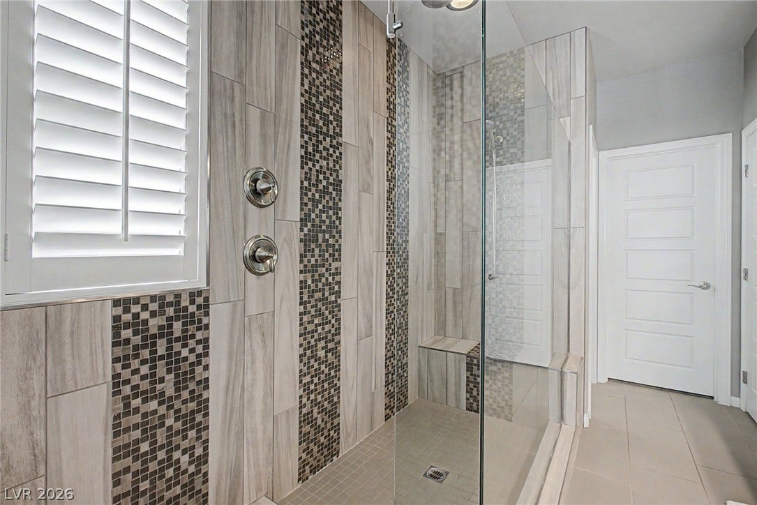 A glass-enclosed shower showcases intricate tilework alongside classic plantation shutters.