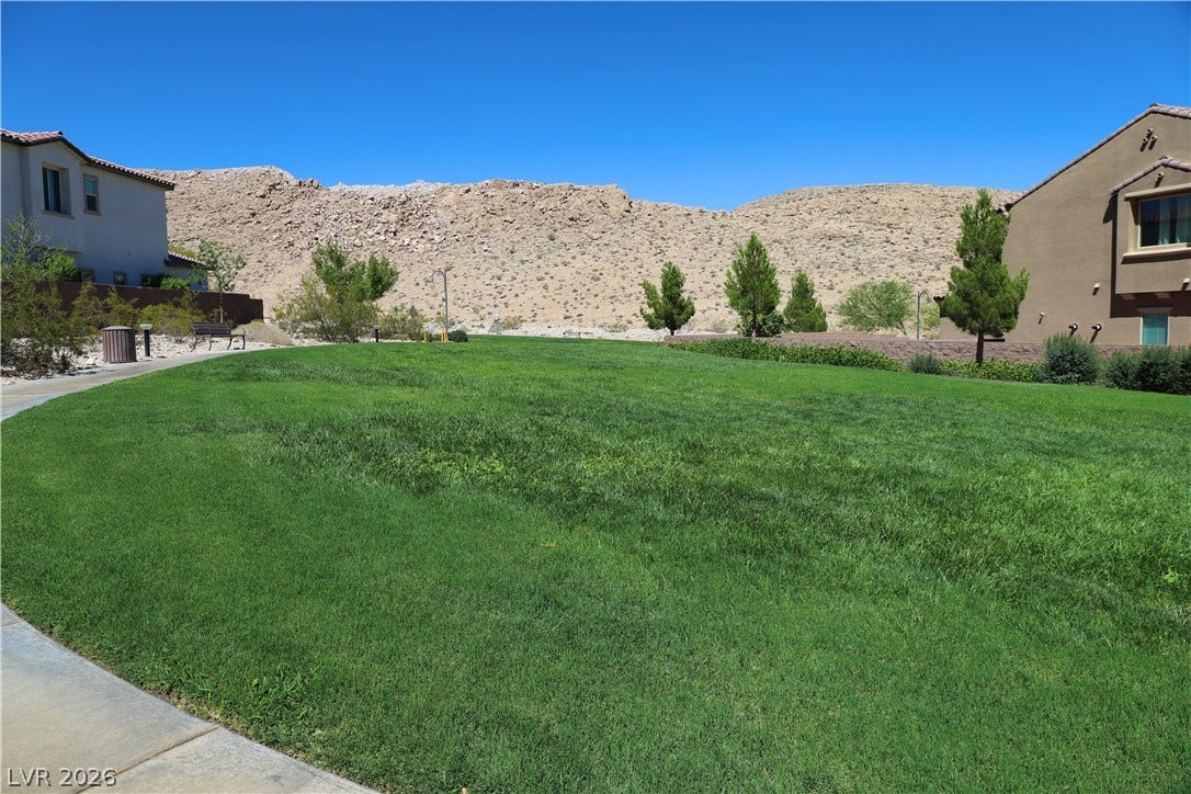 Lush green community space sits framed by rugged mountain vistas and a clear blue sky.