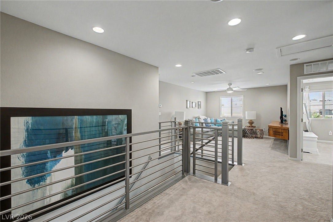 Recessed lighting illuminates a carpeted upstairs loft featuring modern metal stair railings.