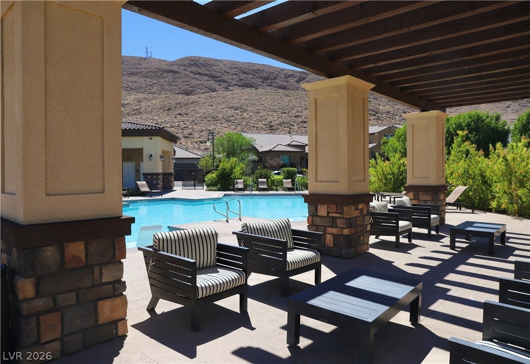 A shaded patio area overlooks the sparkling community pool against a rugged mountain backdrop.