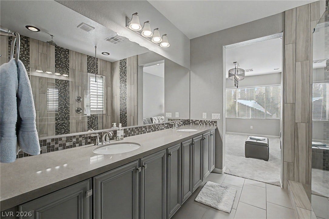 Double vanities with stone counters flank a spacious, modern master bath.