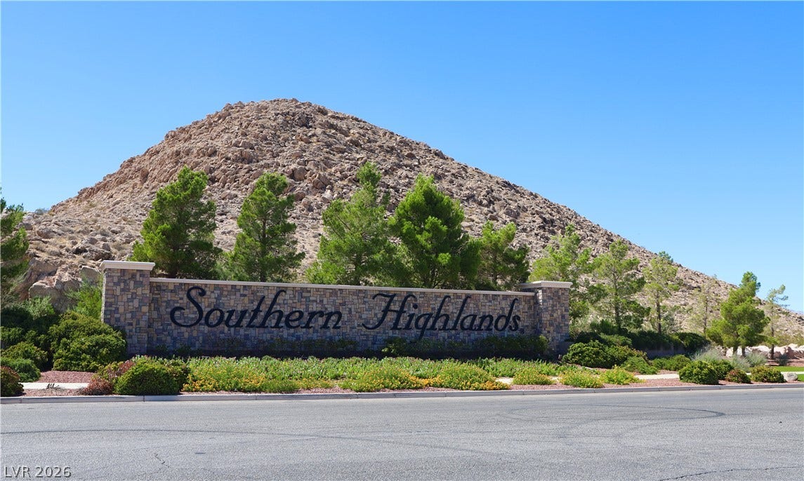 A stone monument sign marks the community entrance set against a rugged desert hillside.
