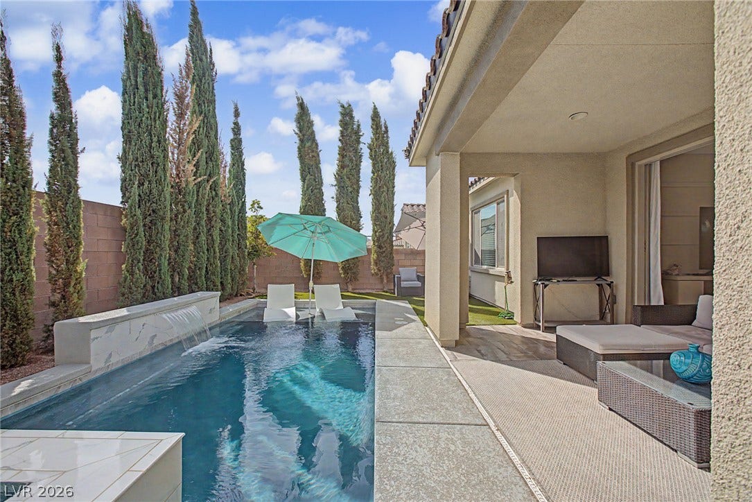 A covered concrete patio overlooks a modern pool accented by a custom waterfall feature.
