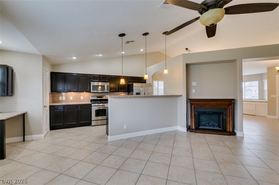 437 Waterwheel Falls Drive, Henderson, NV 89015 Tile flooring pairs with vaulted ceilings and a classic fireplace mantle in this open-concept layout.