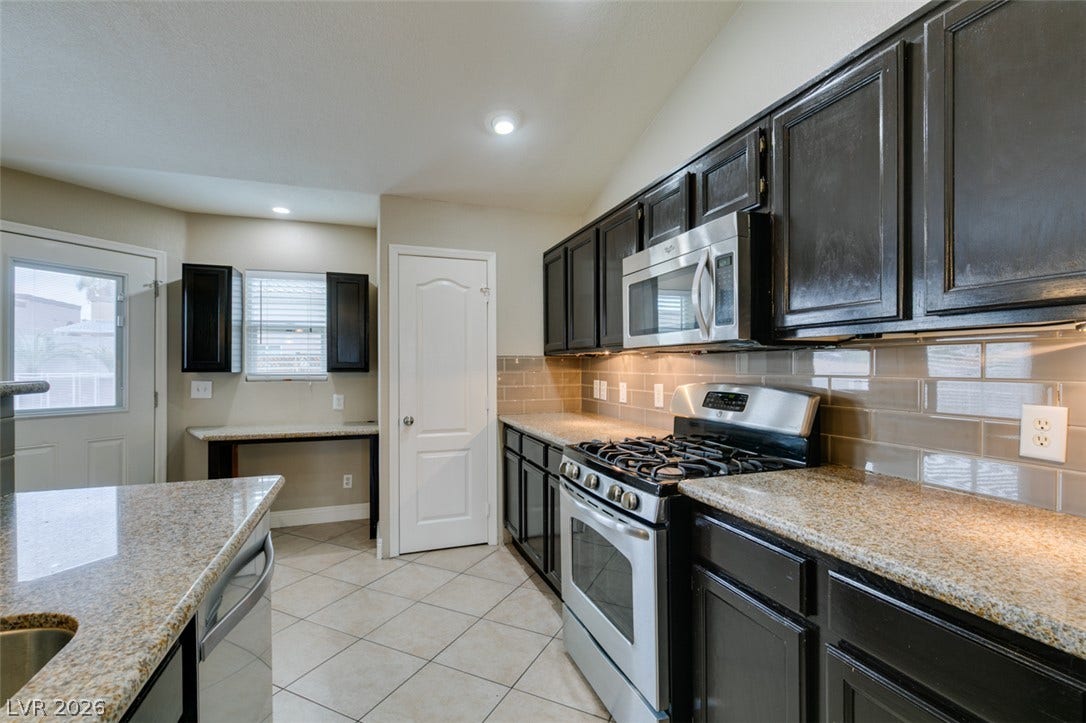 437 Waterwheel Falls Drive, Henderson, NV 89015 Rich dark cabinetry pairs with granite countertops and a tiled backsplash in this kitchen.