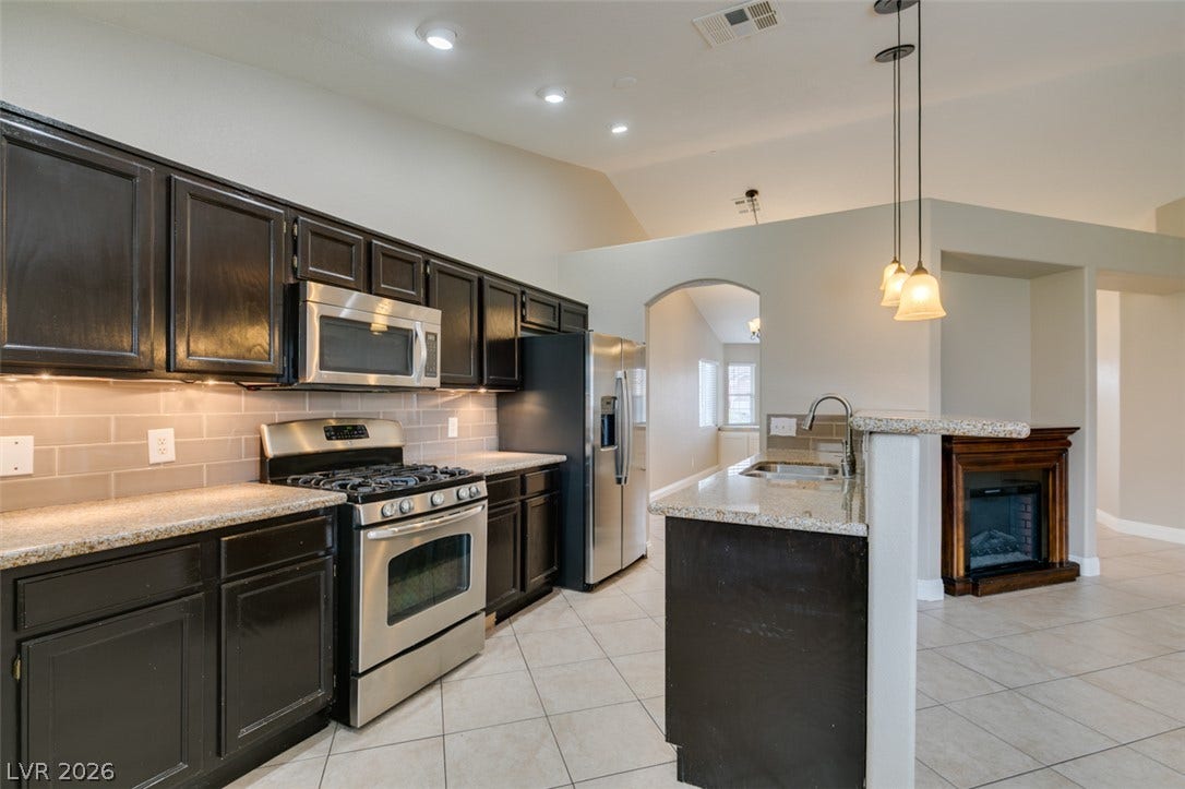 437 Waterwheel Falls Drive, Henderson, NV 89015 Granite counters and dark cabinetry anchor this open kitchen flowing into a tiled living space.