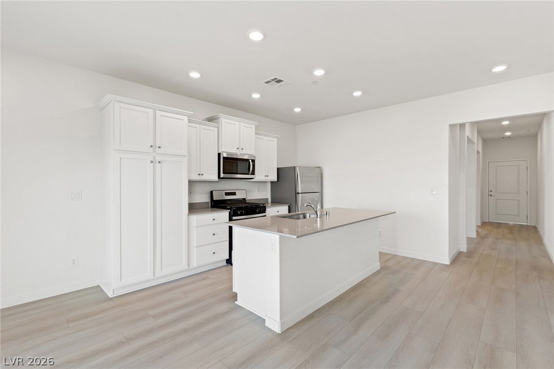 Recessed lighting illuminates this modern kitchen featuring a central island and light wood flooring.