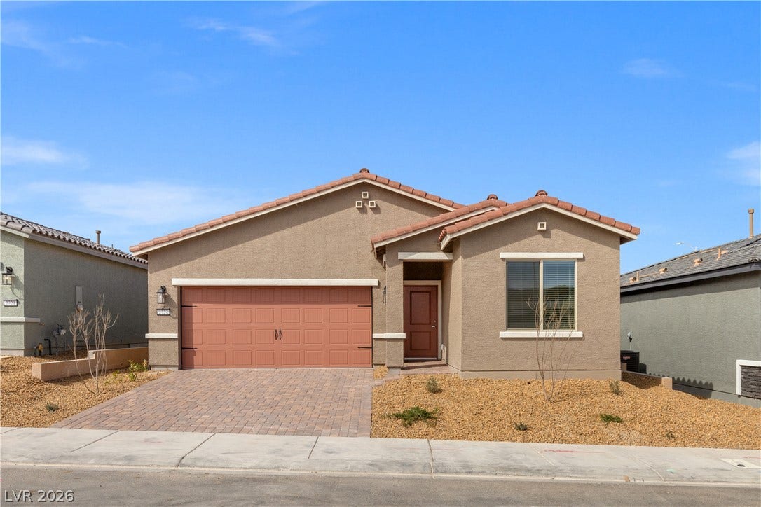 A classic stucco exterior sits behind a paved driveway under clear blue skies.