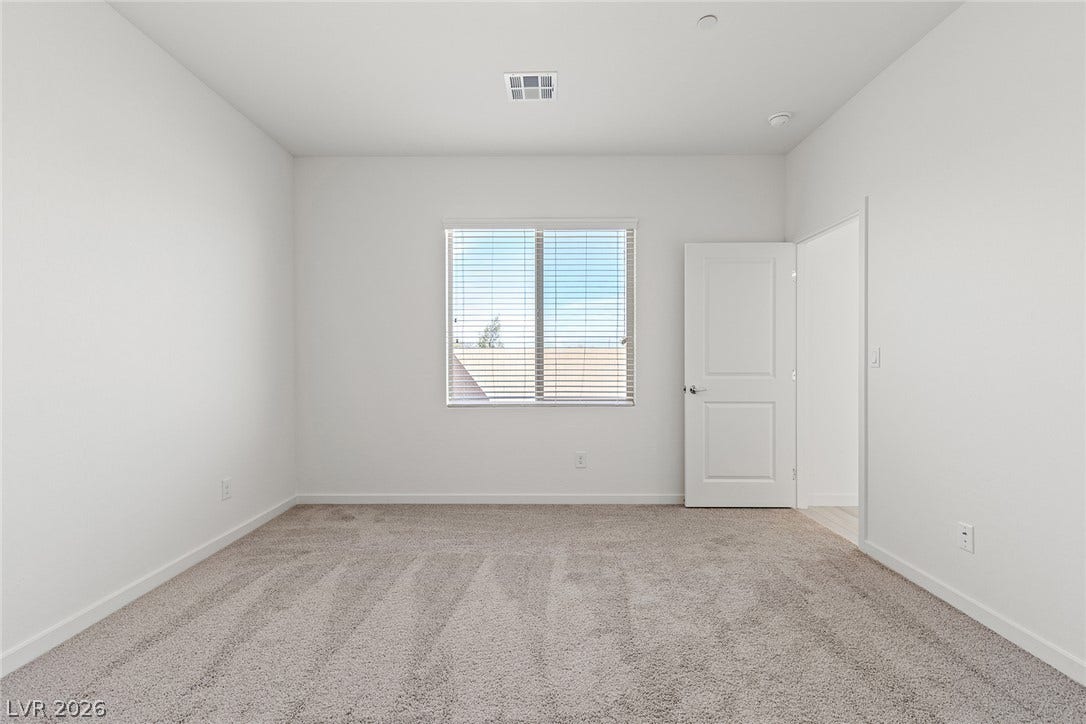 Soft plush carpeting paired with clean white walls and a wide window defines this bedroom.