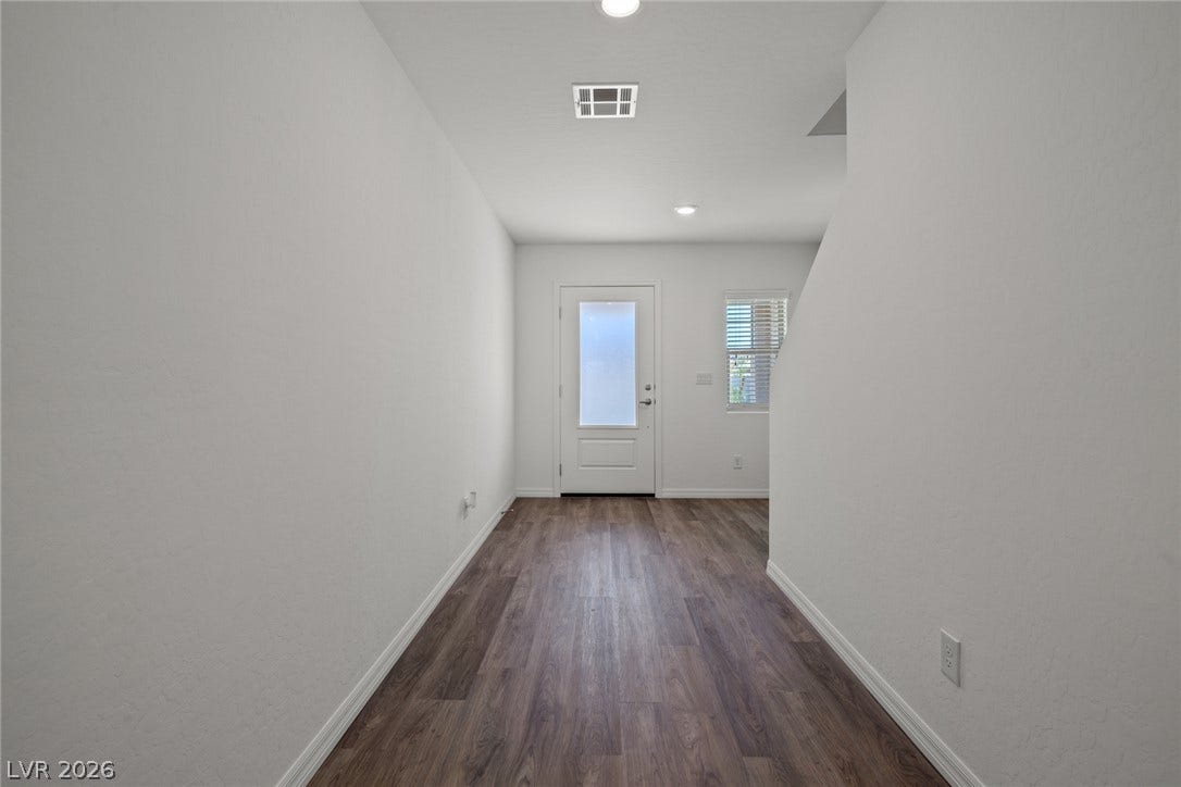 A long hallway with wood-look flooring leads directly toward the front entry door.