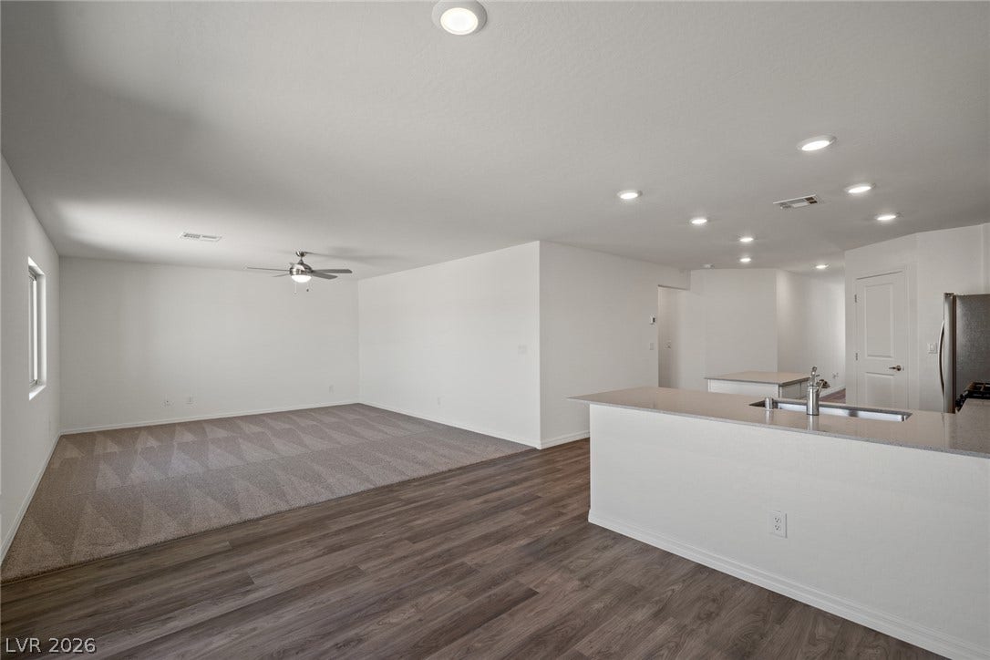 An open floorplan seamlessly connects the stone counters of the kitchen to the carpeted living space.