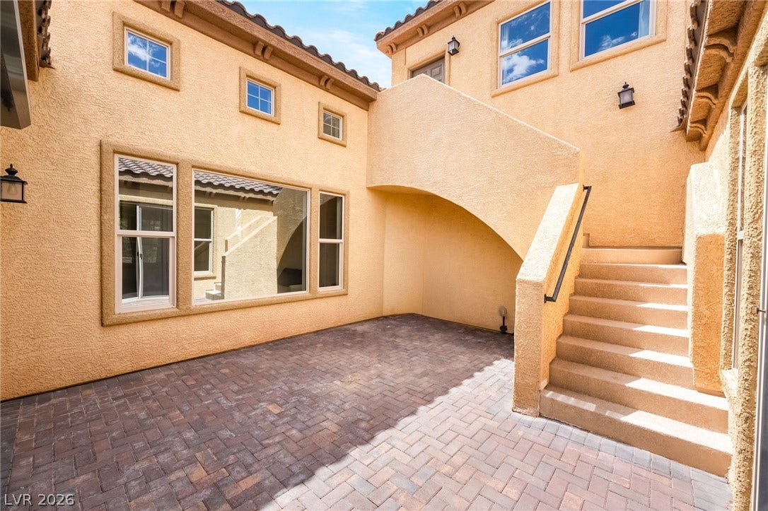 72 Rezzonico Drive, Henderson, NV 89011 An inviting paved courtyard features stucco walls and an exterior staircase under blue skies.