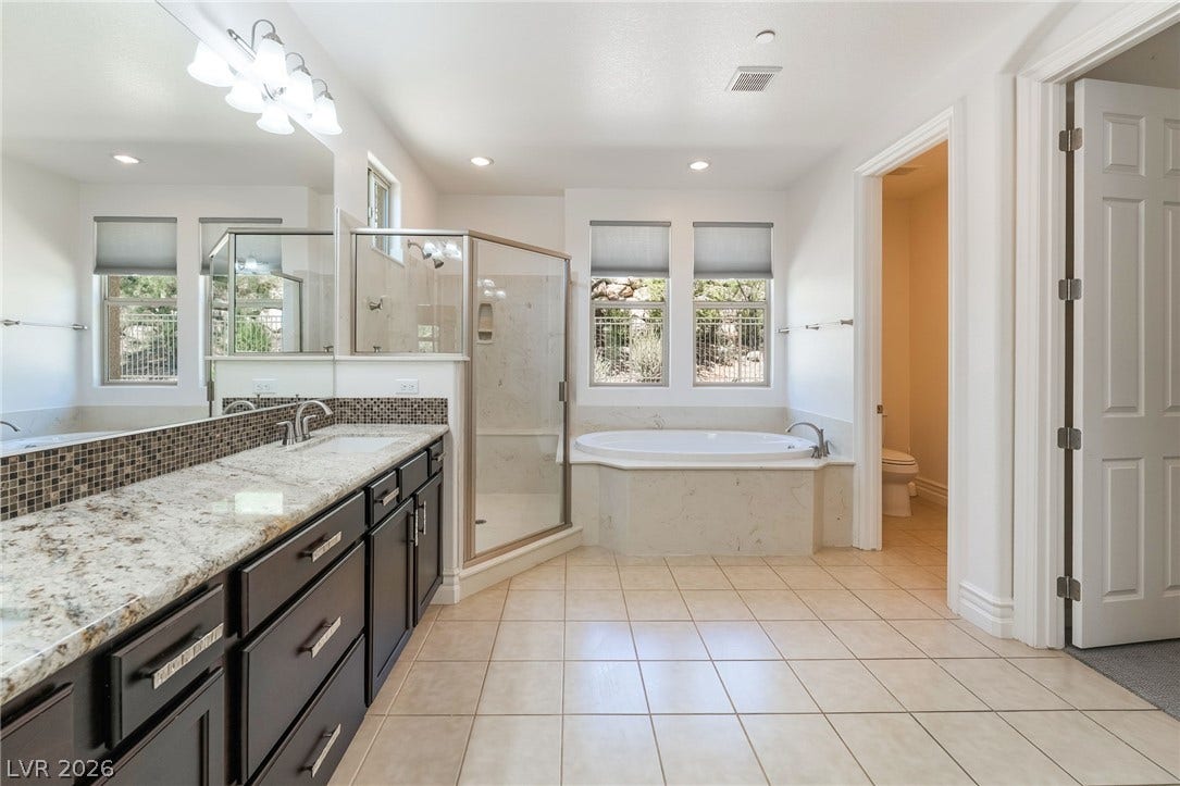 72 Rezzonico Drive, Henderson, NV 89011 A spacious bathroom features a stone-topped double vanity, a soaking tub, and tiled flooring.