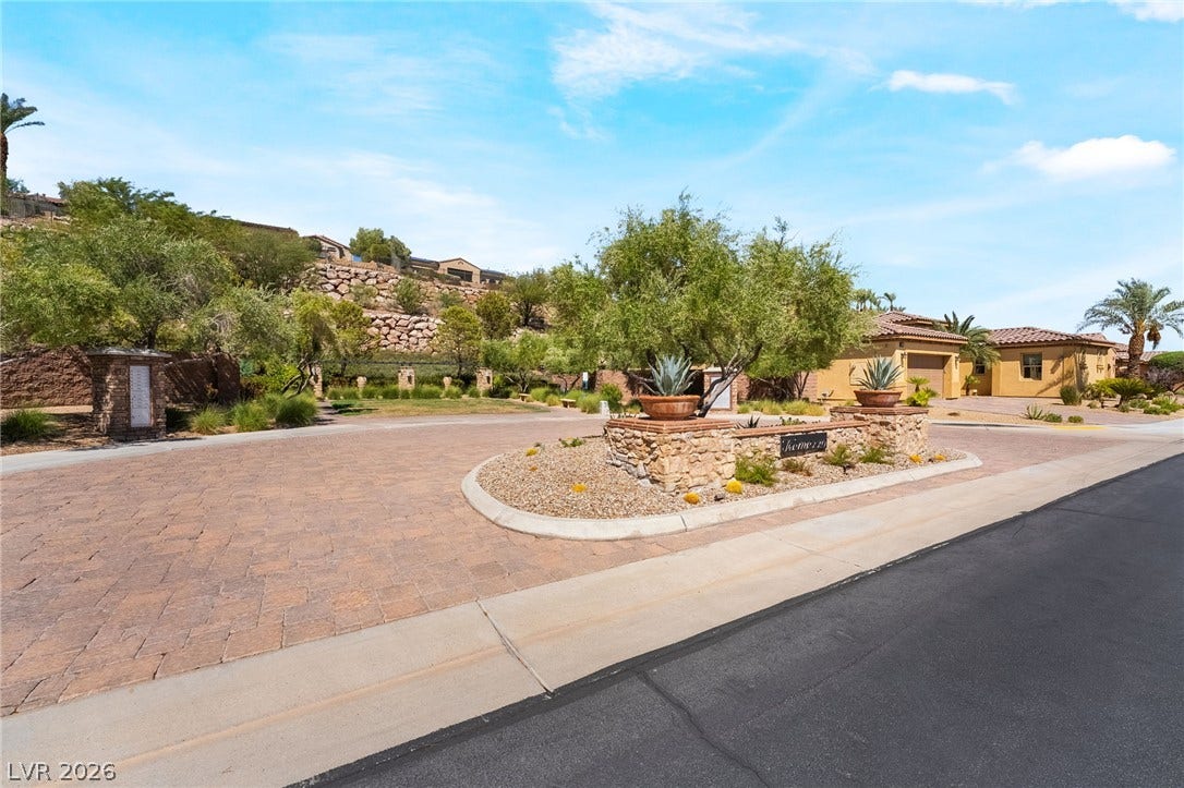 72 Rezzonico Drive, Henderson, NV 89011 An inviting stone-accented entrance driveway leads toward desert landscaping under blue skies.