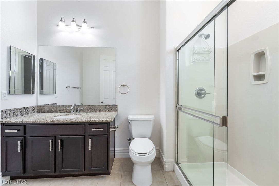 72 Rezzonico Drive, Henderson, NV 89011 A classic bathroom layout pairs dark cabinetry with granite countertops and a glass-enclosed shower.