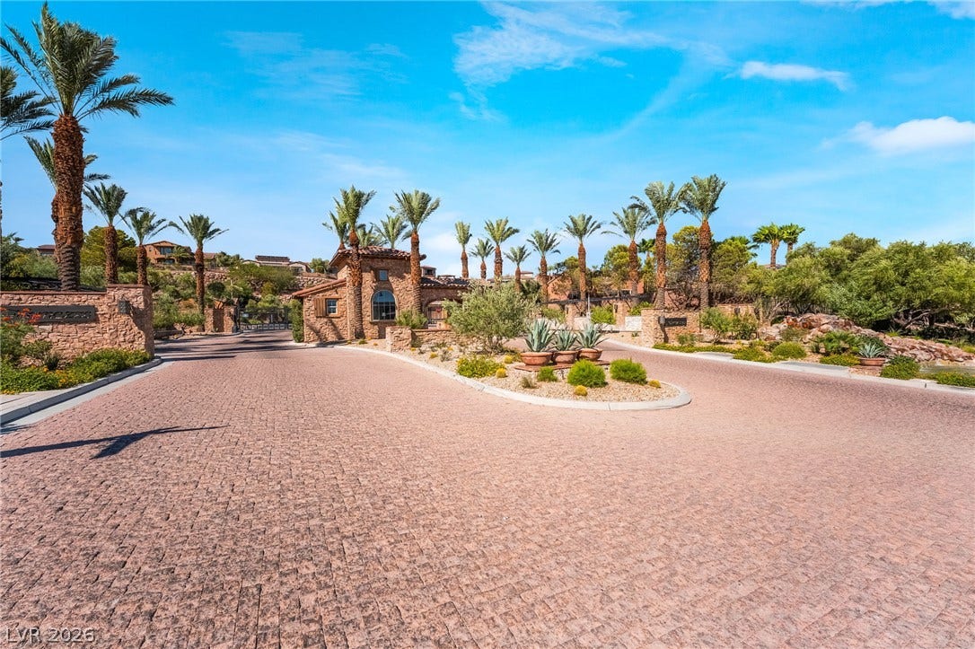 72 Rezzonico Drive, Henderson, NV 89011 An elegant stone gatehouse and paved driveway welcome visitors under a clear blue sky.