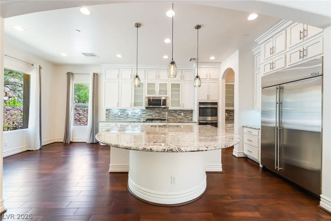 72 Rezzonico Drive, Henderson, NV 89011 Rich hardwood flooring pairs beautifully with white cabinetry and a curved granite kitchen island.