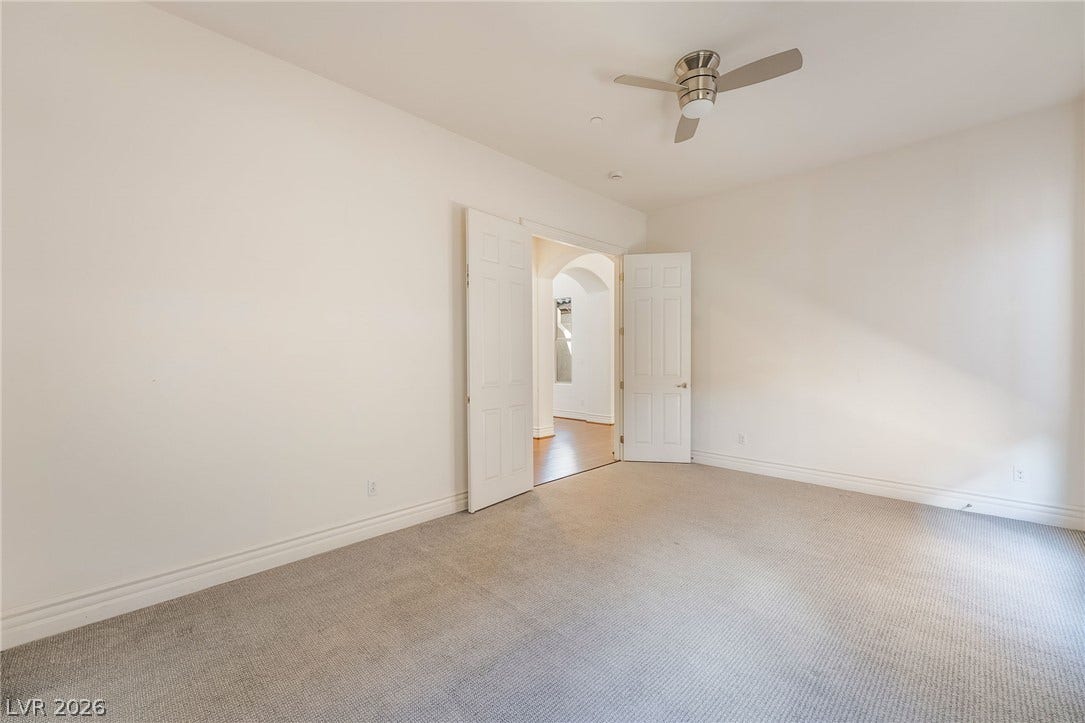 72 Rezzonico Drive, Henderson, NV 89011 Double doors open to a spacious secondary bedroom featuring plush carpeting and clean white walls.