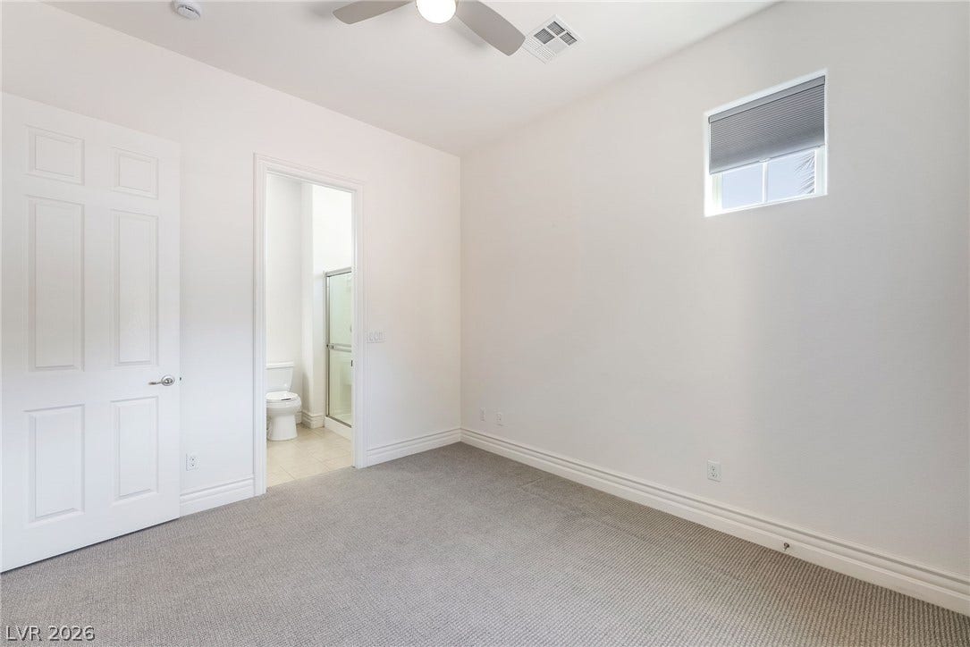 72 Rezzonico Drive, Henderson, NV 89011 A high window illuminates this cozy bedroom featuring soft carpeting and an adjacent bathroom.