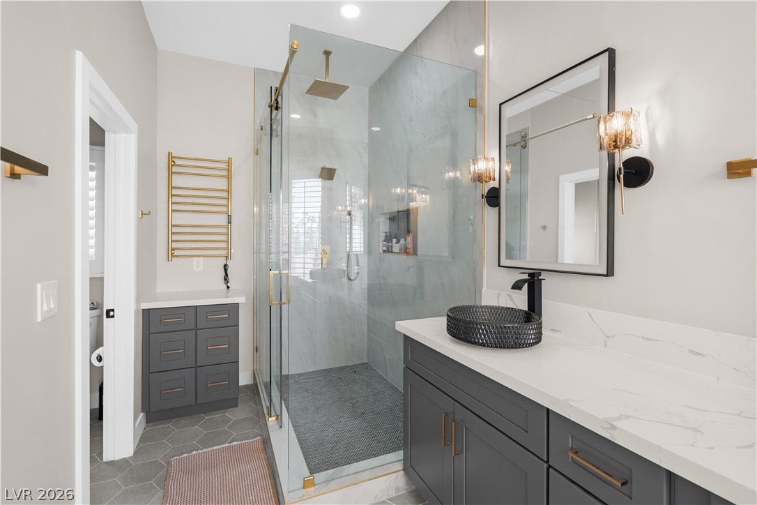 8848 Rainbow Ridge Drive, Las Vegas, NV 89117 Modern stone counters and a sleek glass shower define this contemporary bath space.