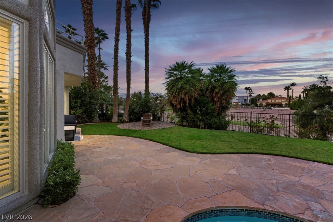 8848 Rainbow Ridge Drive, Las Vegas, NV 89117 An expansive stone patio borders a manicured lawn framed by mature palm trees.