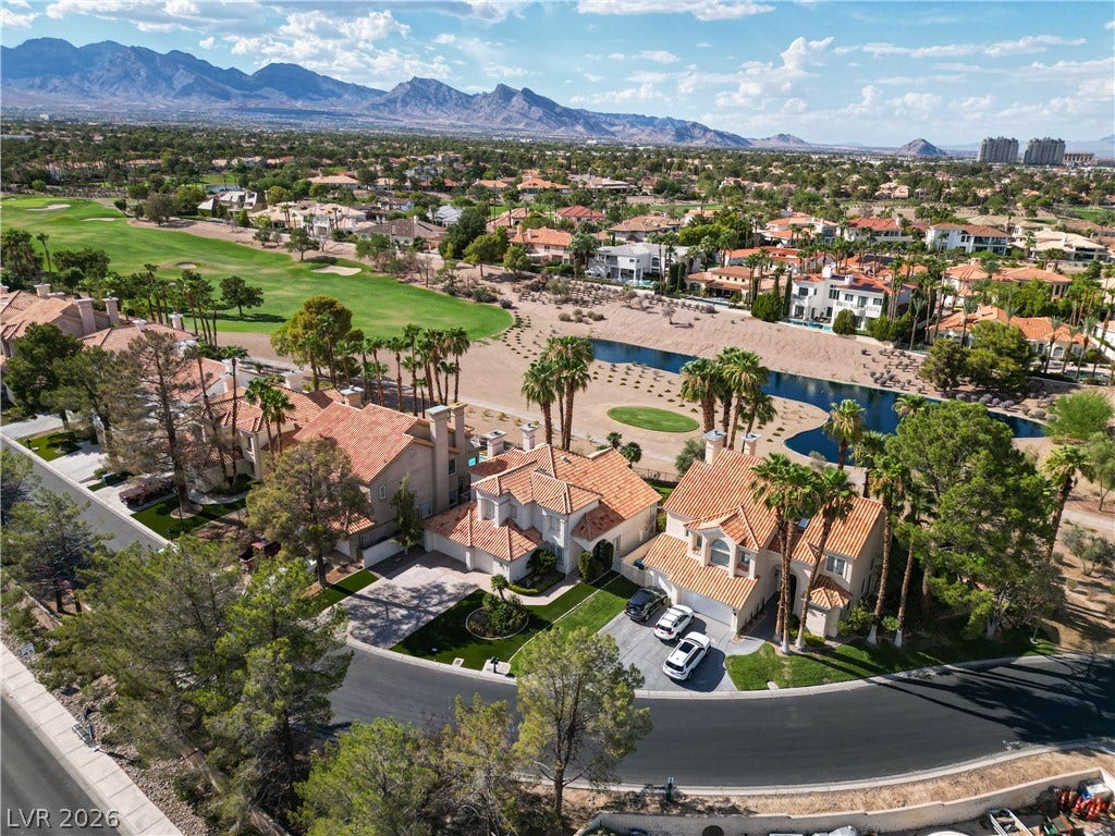 8848 Rainbow Ridge Drive, Las Vegas, NV 89117 Dramatic mountain ranges frame an aerial view of tiled rooftops bordering a green golf course.