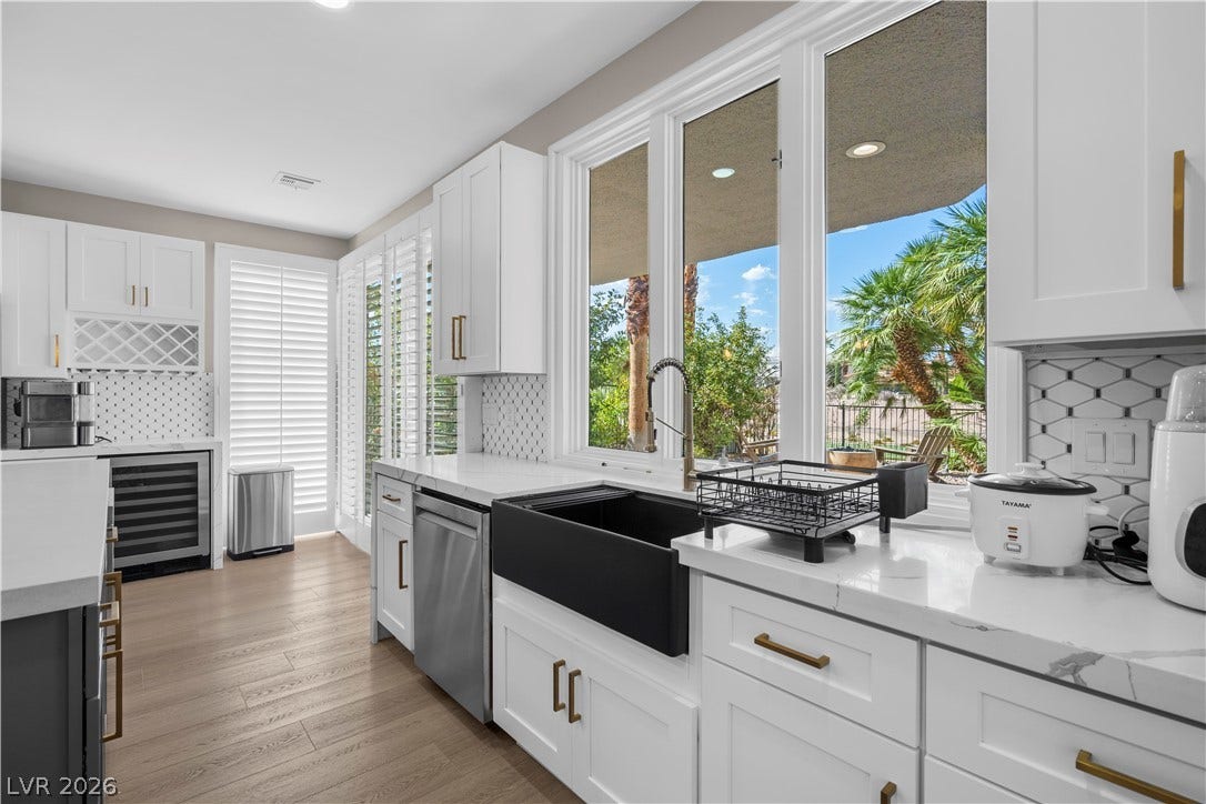 8848 Rainbow Ridge Drive, Las Vegas, NV 89117 Crisp white cabinetry paired with sleek countertops frame a modern farmhouse sink and backyard views.