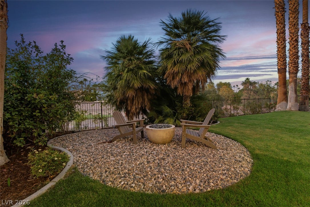8848 Rainbow Ridge Drive, Las Vegas, NV 89117 Lush landscaping and towering palm trees frame a quiet backyard retreat featuring a stone-ringed fire pit.