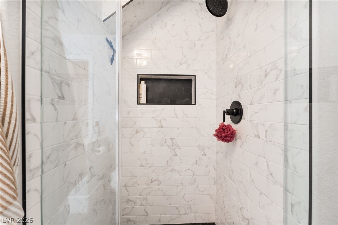 826 Rising Star Drive, Henderson, NV 89014 Floor-to-ceiling marble-patterned tile lines this modern walk-in shower with matte black fixtures.