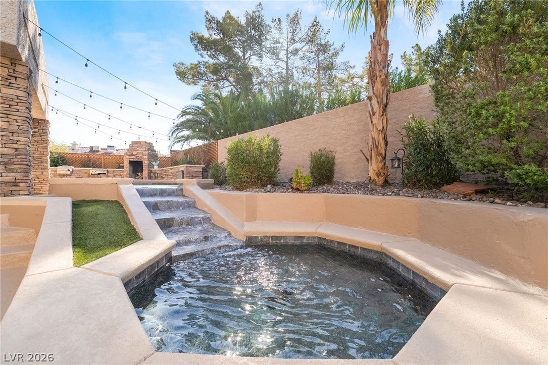 826 Rising Star Drive, Henderson, NV 89014 A stone waterfall cascades into a built-in spa surrounded by concrete decking and privacy walls.