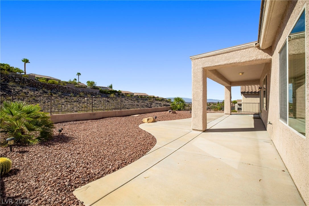2247 Shadow Canyon Drive, Henderson, NV 89044 A covered concrete patio overlooks low-maintenance desert landscaping enclosed by a wrought iron fence.