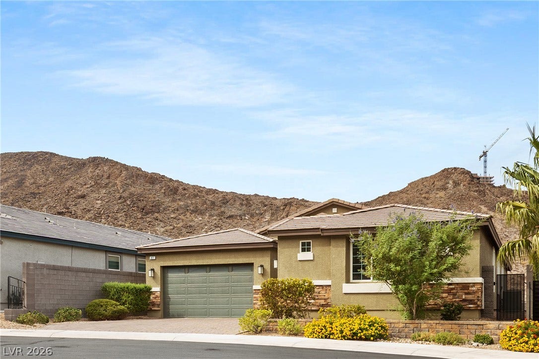 Rugged mountain backdrops frame this modern single-story residence with stone accents and a paved driveway.