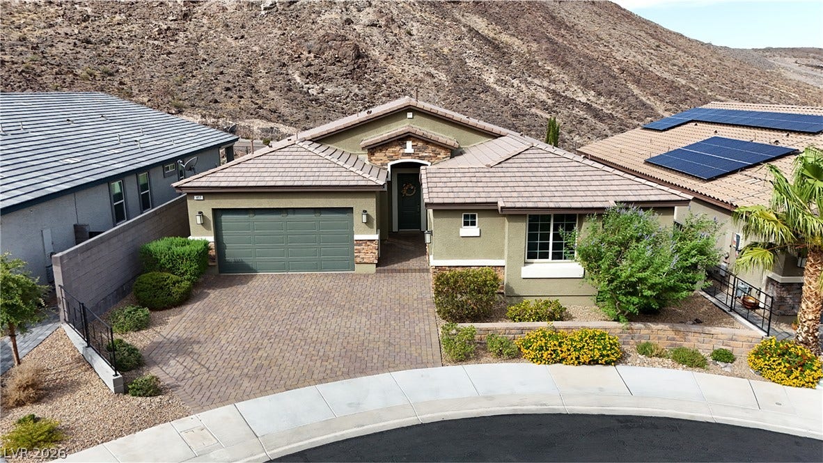 An inviting stone-accented facade leads to a paved driveway nestled against a dramatic mountain backdrop.
