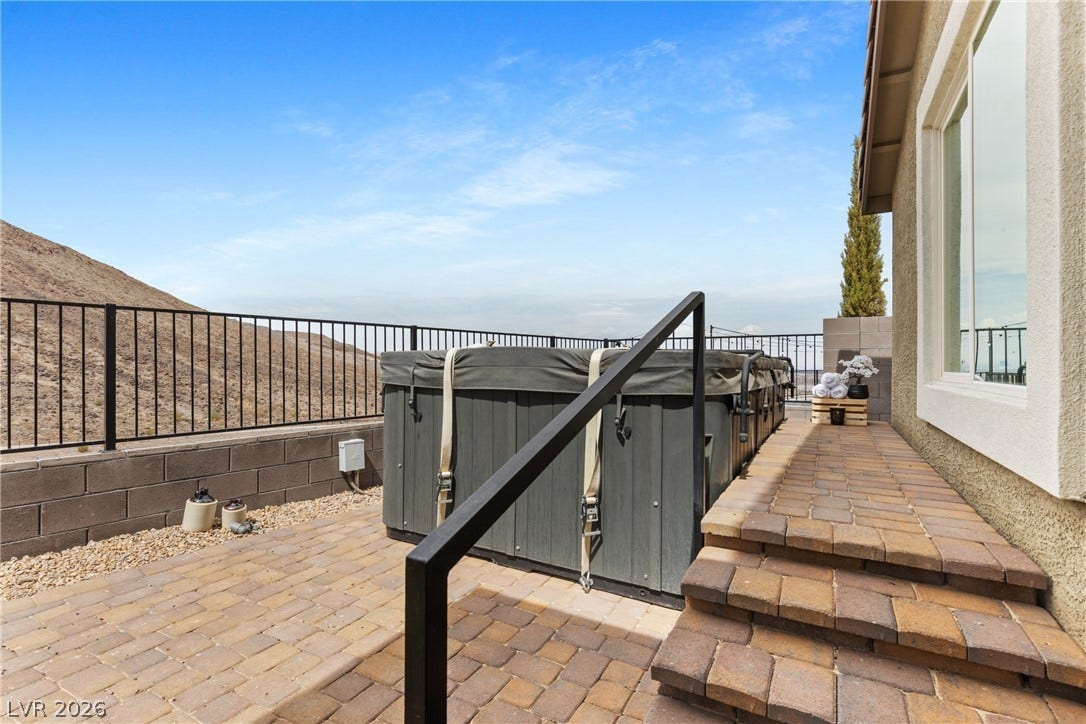 A stone paved patio area frames a private hot tub overlooking scenic hillside views.