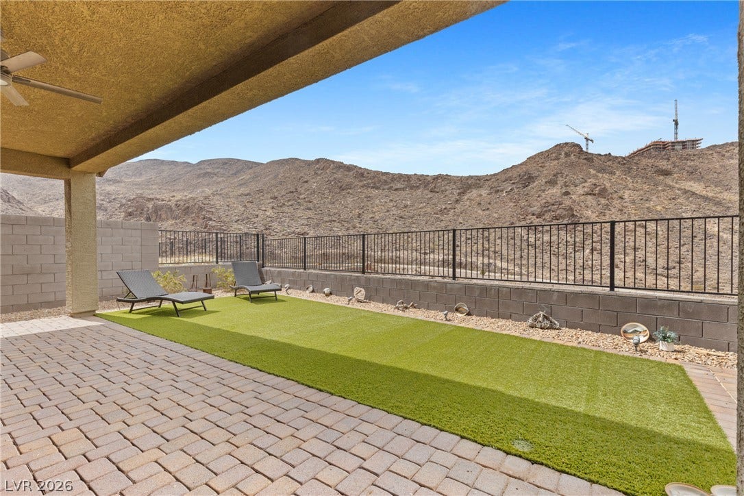 A covered brick patio opens to a fenced lawn with sweeping desert mountain views.