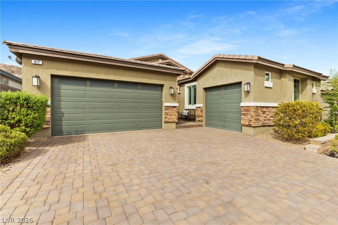 A spacious brick paver driveway leads to the multi-car garage with stone-accented stucco walls.