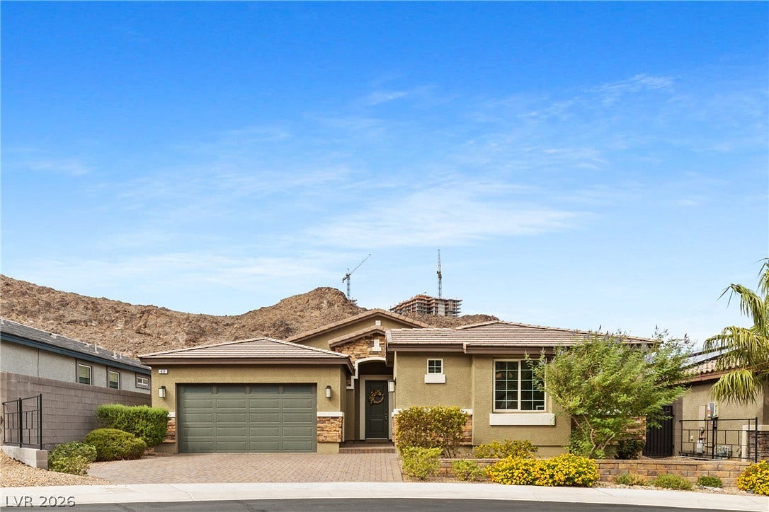 An inviting exterior features a tile roof, paved driveway, and stone accents against desert hills.