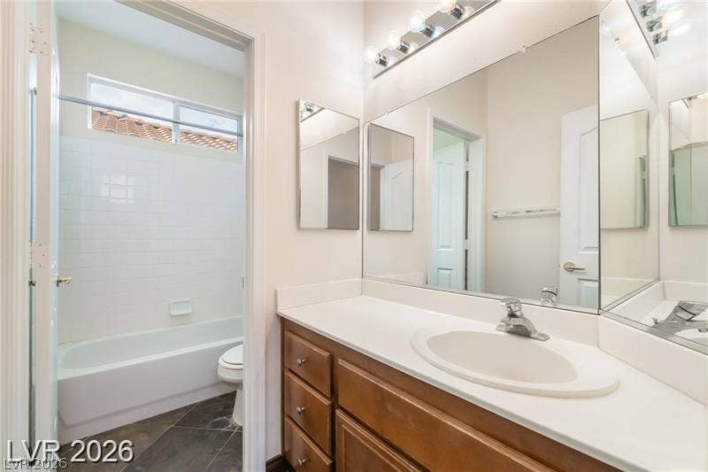 10605 Bardilino Street, Las Vegas, NV 89141 Dark tile flooring accents this bathroom featuring a white vanity top and tub surround.