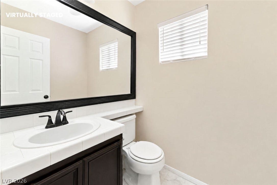 1874 Mesquite Canyon Drive, Henderson, NV 89012 A classic tiled vanity and large dark-framed mirror anchor this elegant powder room.
